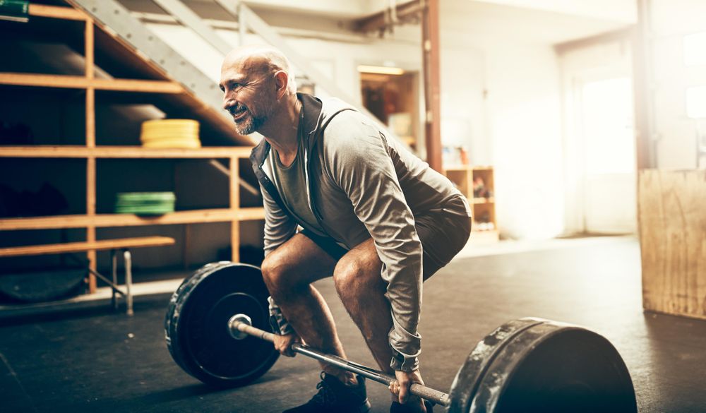 Fit man in grey hoodie deadlifting barbell