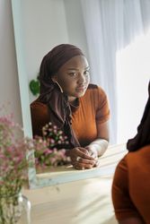 Pensive Black female in hijab looking in mirror