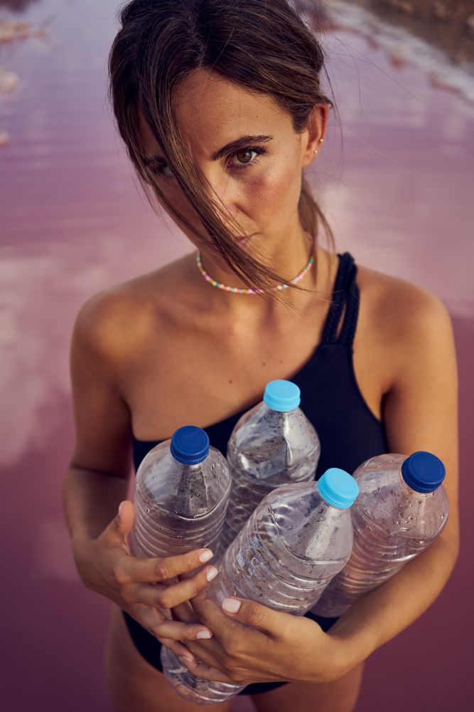 Concerned female in swimsuit collecting trash in natural lake