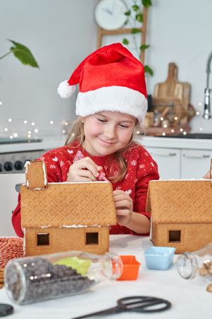 Girl in Santa hat making gingerbread house
