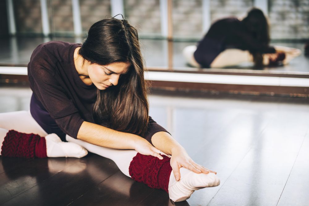 Young woman practicing ballet and flexing muscles sitting on studio floor.