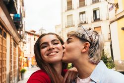 selfie photo of two young women kissing on the cheek