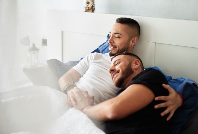 Smiling gay couple hugging on bed