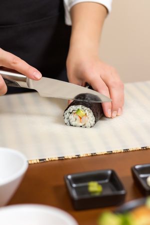Female chef cutting Japanese sushi rolls with rice, avocado and shrimps in nori seaweed sheet, vertical