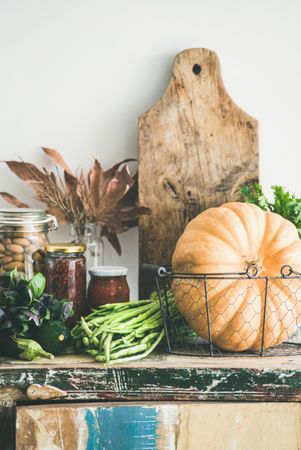 Fresh autumnal produce on kitchen counter, with squash and wooden board with fall leaves