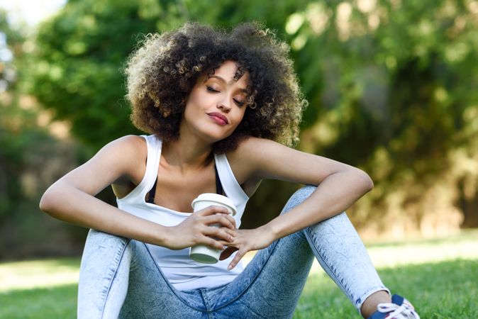 Black woman with afro hairstyle relaxing in park with coffee