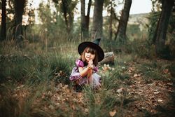 Girl in witch costume crouched down in the forest with finger to her mouth