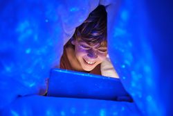 Cheerful boy browsing tablet under blanket
