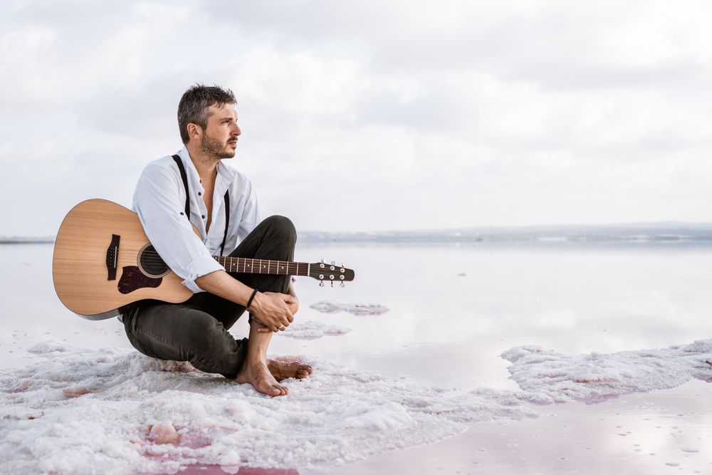 Musician with guitar on pink sandy water