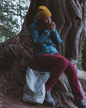 Woman sitting on tree root and warming hands