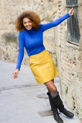 Smiling female with curly hair wearing bright blue shirt holding bars on window on street