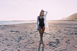 Young woman standing on beach with sunset at her back holding her hair