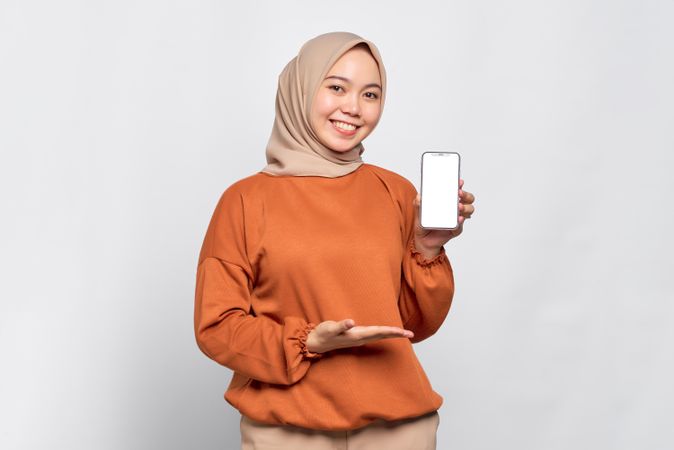 Muslim woman smiling while holding up smart phone mock up screen