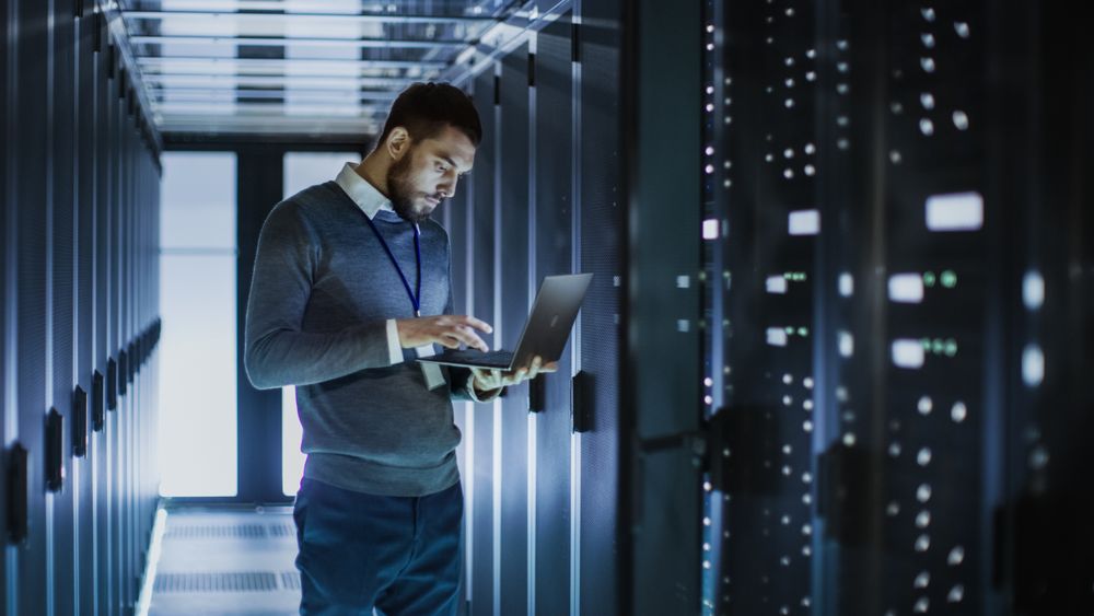 IT Technician Works on Laptop next to a Server Cabinet in Big Data Center.