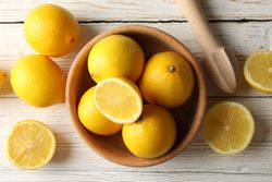Bowl, lemons and wood juicer on wooden background, top view