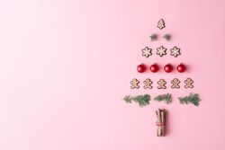 Christmas tree made with evergreen fir, bauble decoration and winter cookies on pink background