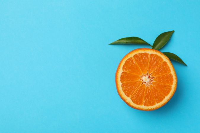Half of mandarin with leaves on blue background Half of mandarin with leaves on blue background