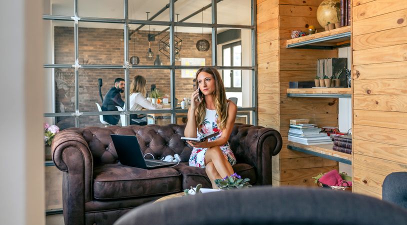 Woman working with laptop talking on the phone sitting on the sofa