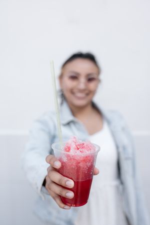 A young Hispanic woman is smiling while drinking a Mexican cherry slushy outdoors