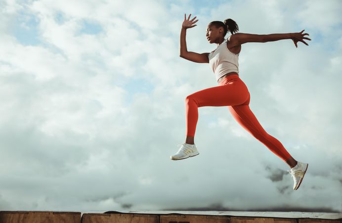 Female athlete doing jumping workout on building terrace