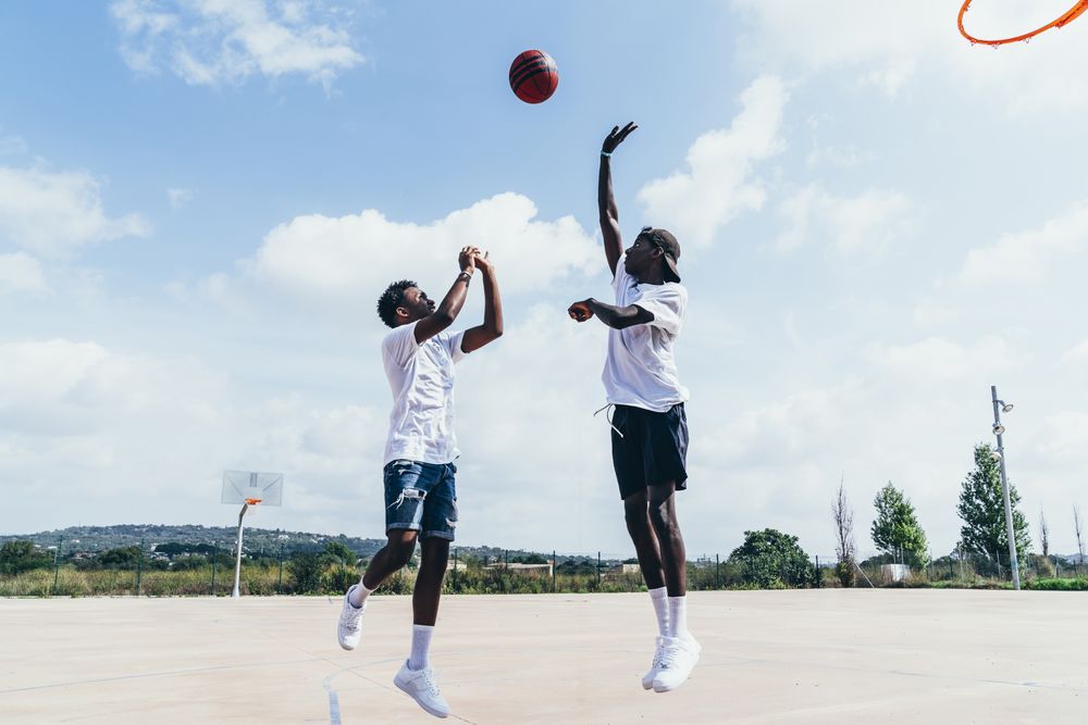 Black men playing basketball in bright day