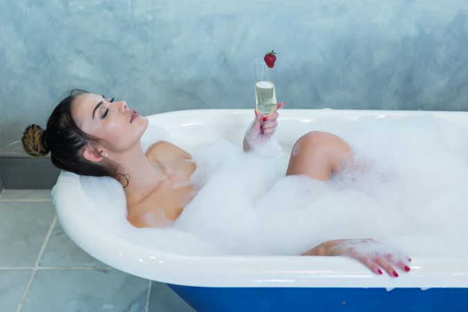 Woman holding a glass of champagne in a bathtub