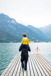 Man with kid on neck walking along pier