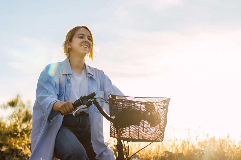 young blonde woman cycling in a field at sunset
