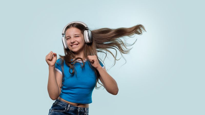 Girl happily dancing with headphones, hair flying mid-movement.