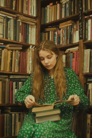 Girl in green polka dress reading a book in library