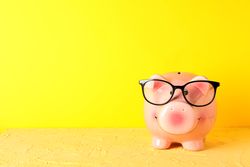 Happy piggy bank with glasses on color table against yellow background, space for text. Finance, saving money