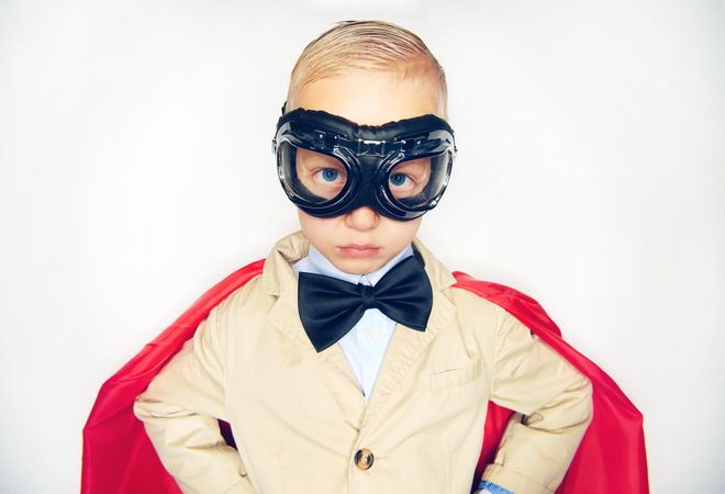 Unsmiling blond boy wearing airplane goggles and cape
