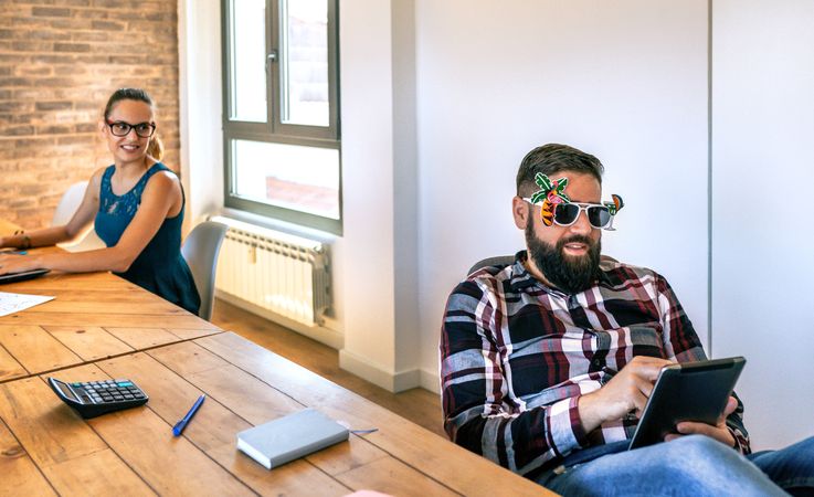 Businesswoman looking at her colleague who is wearing funny glasses because he is going on vacation