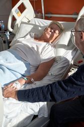 Older man holding hand of parient lying on bed in hospital