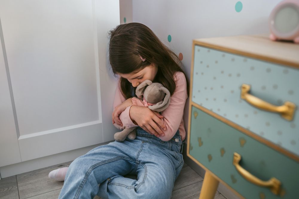 Unhappy girl hugging stuffed toy sitting on the floor