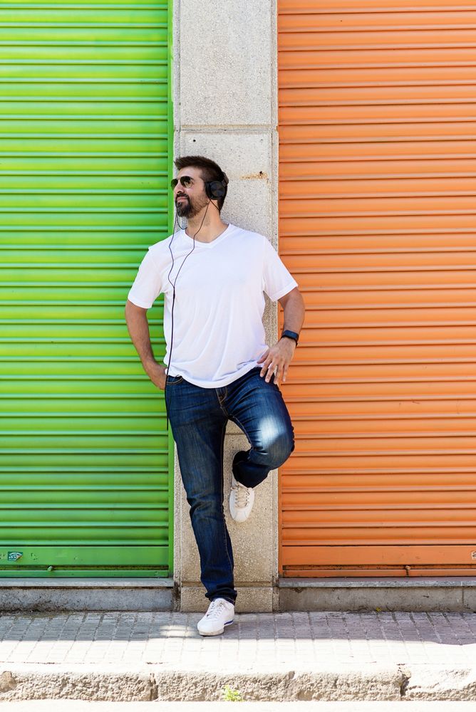 Man listening to music on headphones leaning on wall between colorful shutters