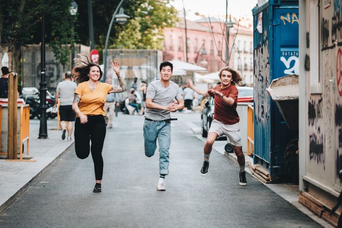 Funny multiracial friends having fun and running along city street