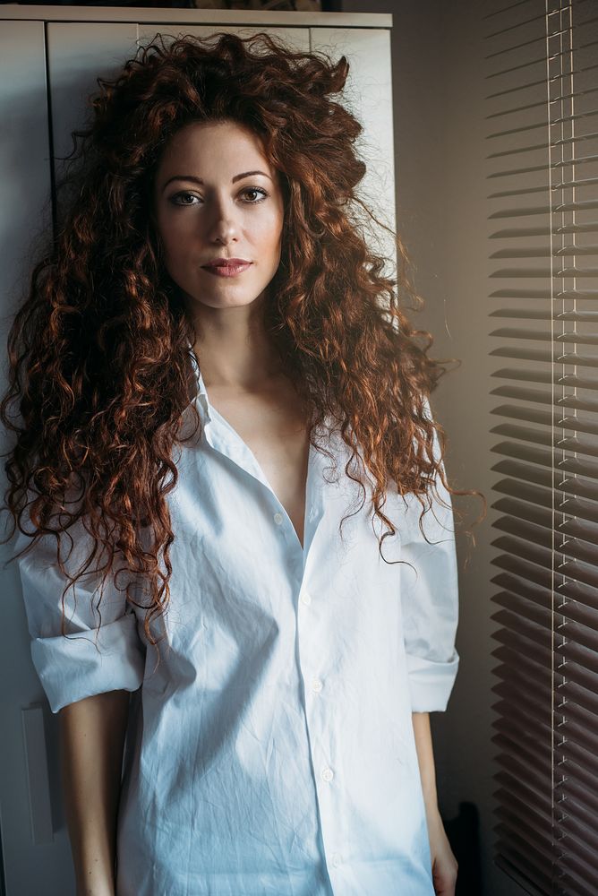 Beautiful thoughtful woman standing by a windows blind