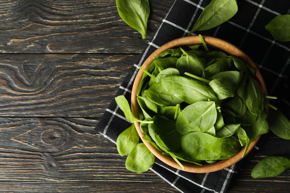Wooden bowl with spinach and napkin on wooden background