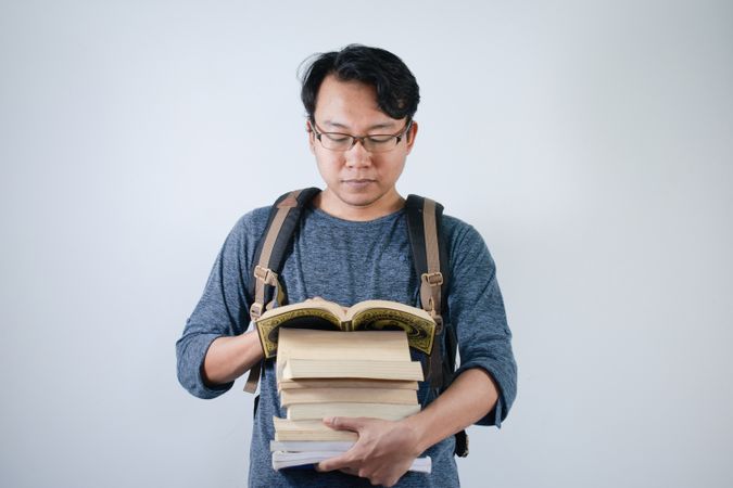 Asian young male student wearing bag and carrying books smiling and happy expression