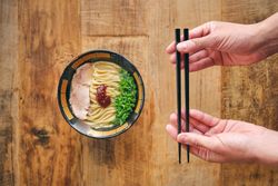 Crop person with chopsticks above tasty ramen on desk