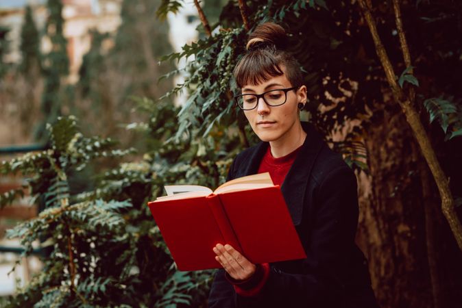 Young woman reading book on bench in park