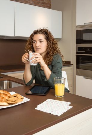 Woman holding coffee over tablet screen at breakfast