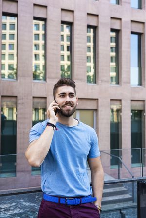 Portrait of smiling modern man speaking by phone leaning outside