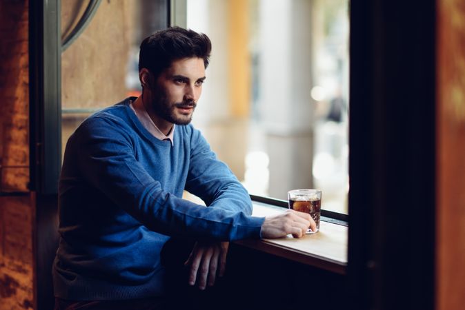 Man with blue sweater sitting with a drink in a modern pub