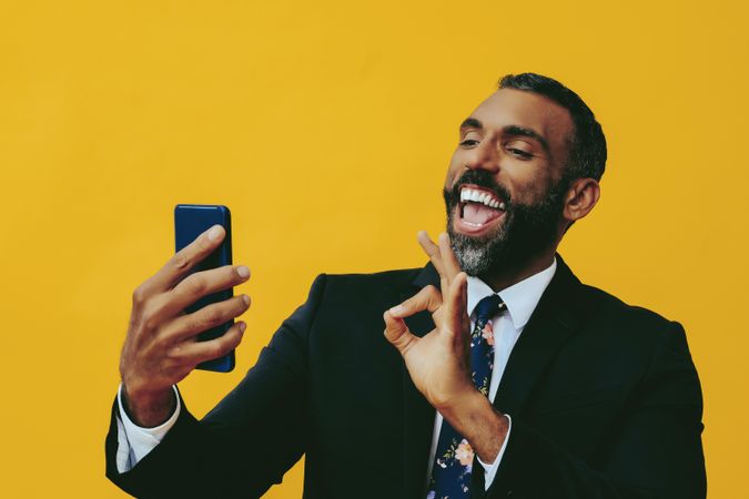 Energetic Black businessman in suit gesturing at smartphone screen