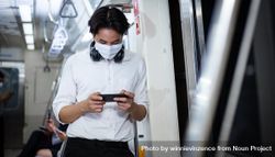 Man in facemask and headphones looking at smartphone in metro car 4Oa6J0