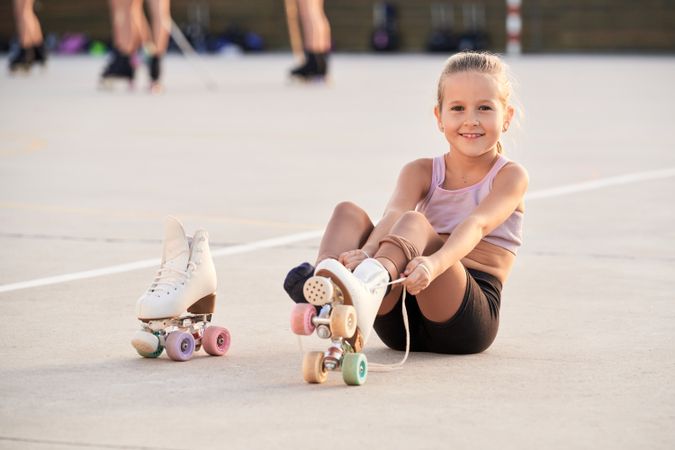 Cheerful child putting on roller skates in city