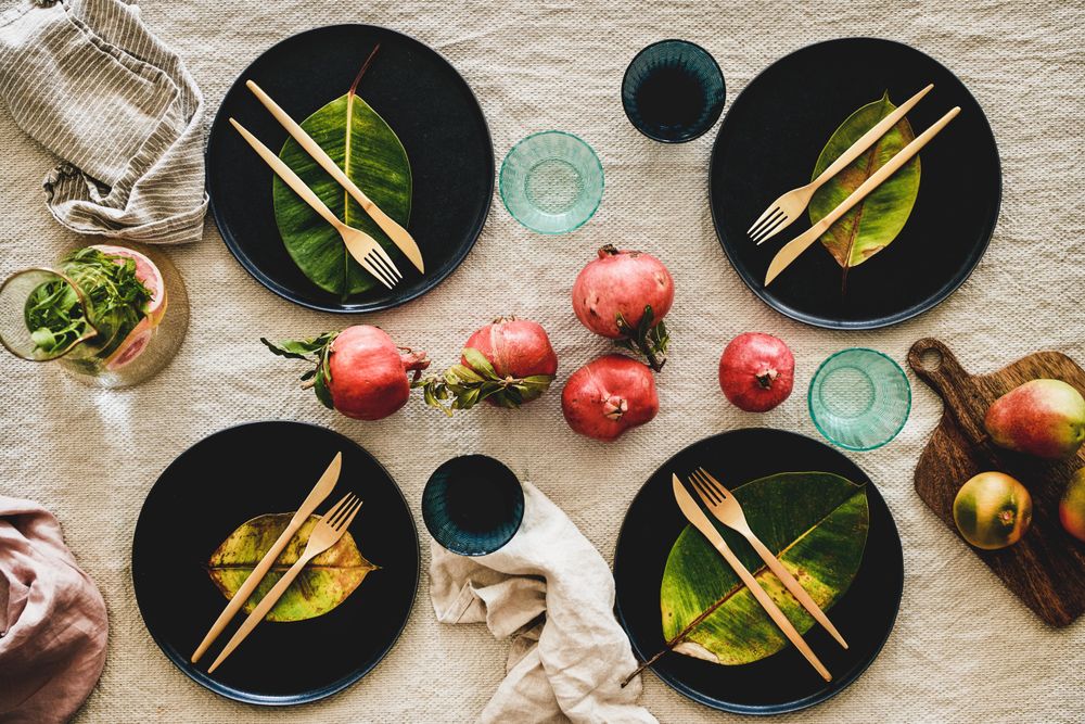 Fresh table setting on brown table cloth, leaves on dark plates, pomegranate