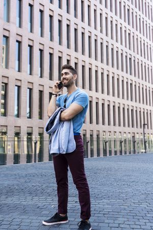 Portrait of cheerful modern businessman speaking by phone and smiling while standing outdoors